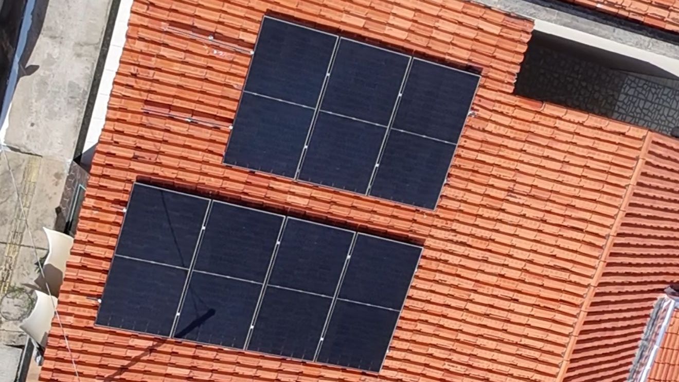 Vista aérea de uma residência com dois arranjos de módulos fotovoltaicos no telhado cerâmico.